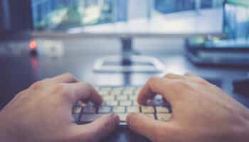 Hands are typing on a white keyboard, screen in the blurry background