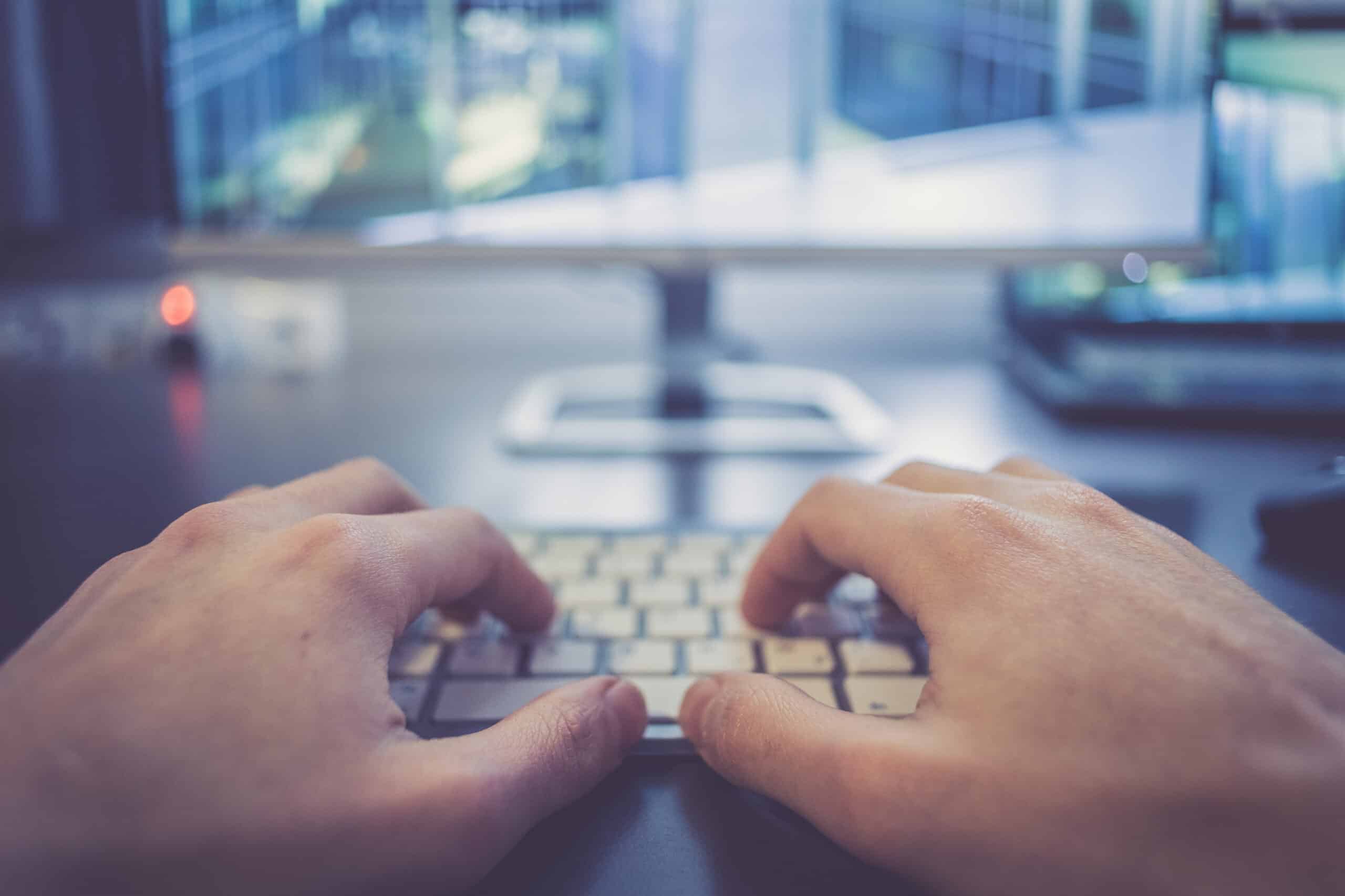 Hands are typing on a white keyboard, screen in the blurry background